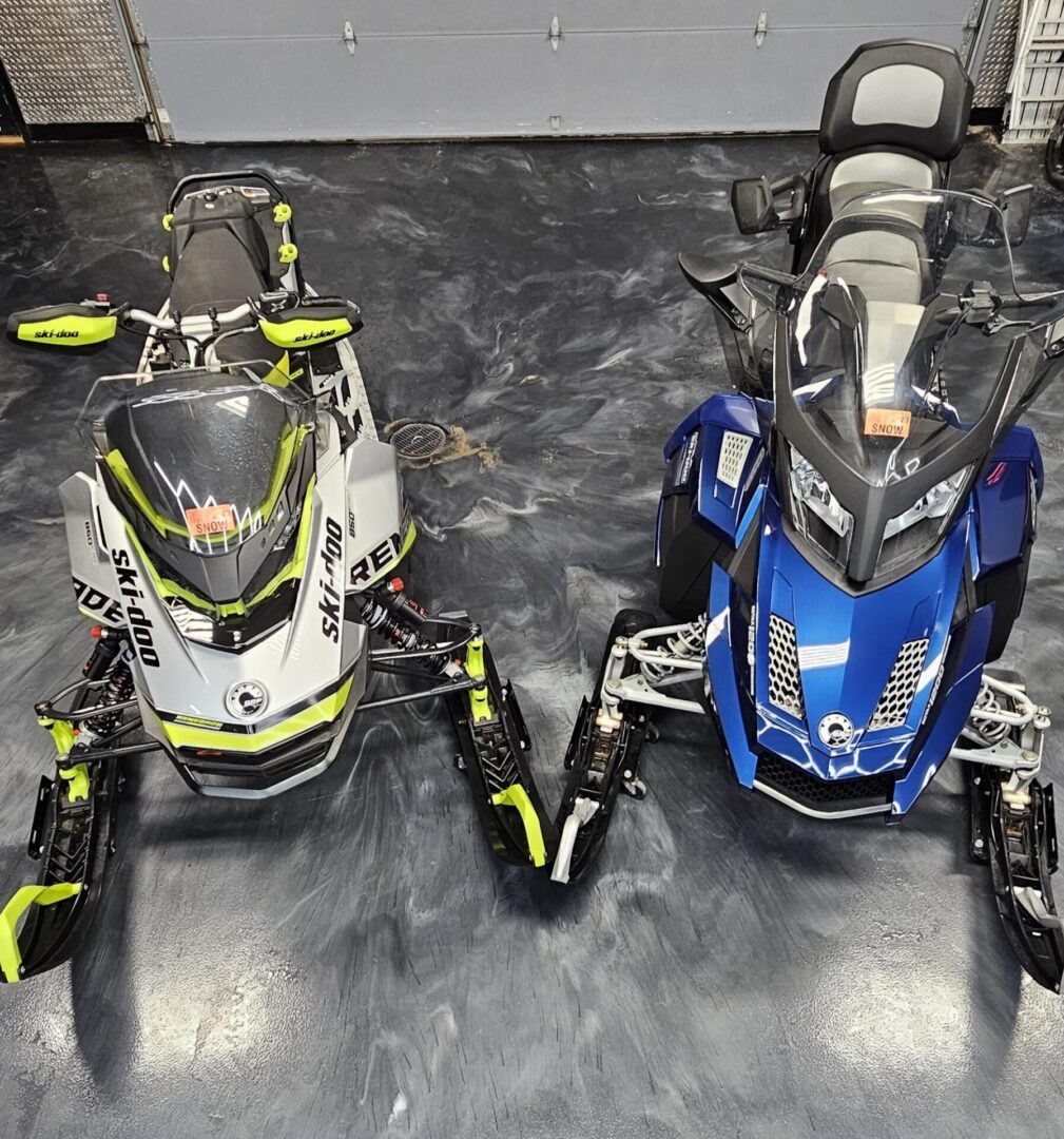 Two snowmobiles are parked on the floor of a garage.